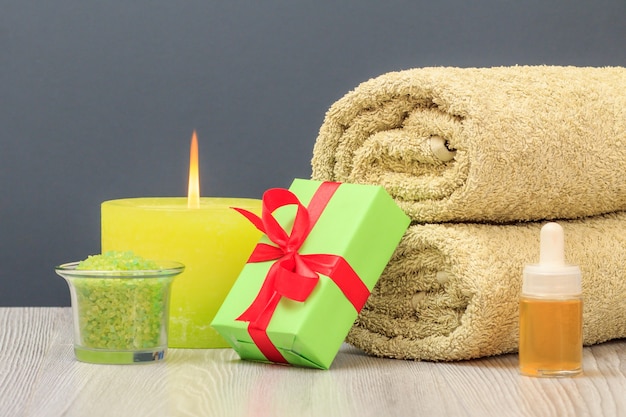 Spa composition with soft terry towel, gift box, bowl with sea salt, bottle of aromatic oil and burning candle on gray background.