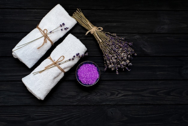 Spa concept. Lavendelzout voor een ontspannend bad, witte handdoeken en droge lavendelbloemen op een zwarte houten achtergrond. Aromatherapie plat lag.