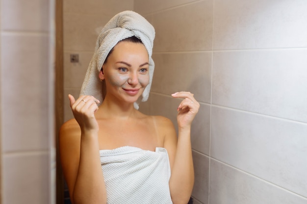 Spa and cosmetology facial skin care at home girl in the bathroom applies a cream face mask