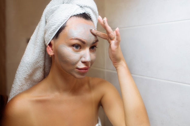 Spa en cosmetologie gezichtsverzorging thuis meisje in de badkamer brengt een crème gezichtsmasker aan