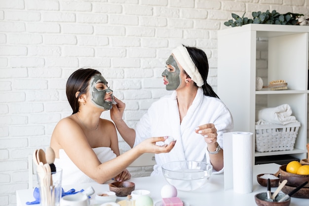 Spa- en wellness-concept. Zelfzorg. twee mooie vrouwen in badjassen gezichtsmasker met plezier toe te passen