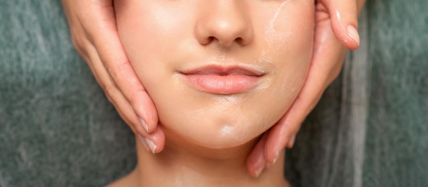 Spa facial skincare. Close-up of a young caucasian woman getting spa moisturizing face massage treatment at beauty spa salon.