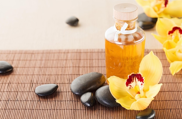 spa, health and beauty concept - closeup of essential oil, massage stones and orchid flowers