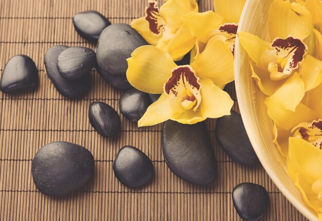 spa, heath and beauty concept - massage stones with orchid flowers on mat