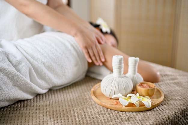 Spa herbal balls and spa salt on massage table with a lady\
receiving massage on the massage table