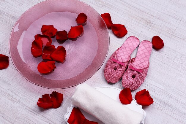Spa kom met water, rozenblaadjes, handdoek en slippers op lichte achtergrond. Concept van pedicure of natuurlijke spabehandeling