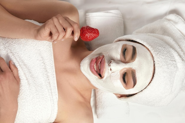 Spa mask beautiful woman with a clay mask on her face and
strawberry in hands face peeling mask