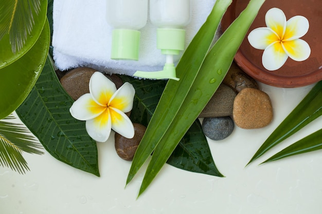 Spa of wellness achtergrond met witte handdoeken tropische bladeren stenen bloemen lichaam en gezichtsverzorging tools en accessoires op witte achtergrond bovenaanzicht