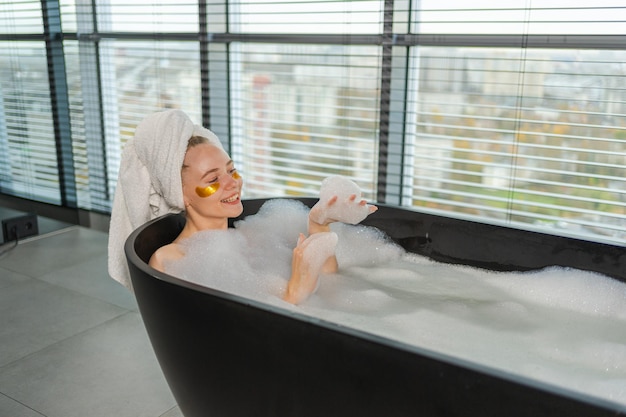 Spa ontspanning jonge vrouw liggen in het bad met schuim bubbels meisje ontspannen in de badkamer thuis mooi