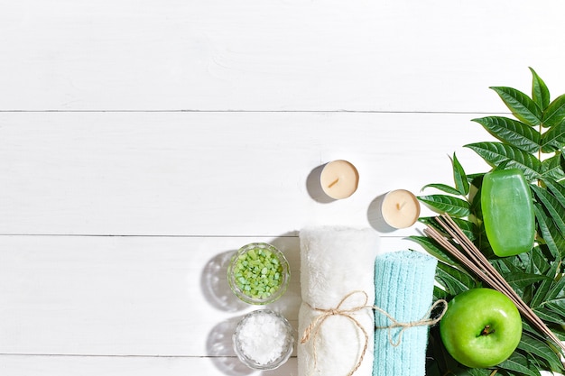 Спа-продукты соли для ванн, мыльные свечи и плоское полотенце на белом деревянном фоне, вид сверху