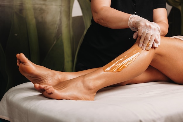  spa professional having a sugaring session on legs for a charming woman