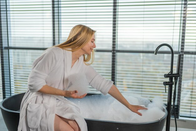 Spa relaxation young woman in spa bathrobe sitting at bath with foam in bathtub girl relaxing in