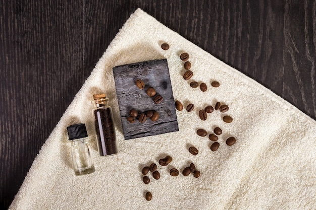 Photo spa set in brown: natural soap, aromatic oil, coffee beans and towel on wood background.