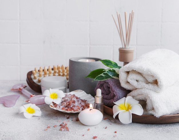 Spa set, essential oil, massage salt, candle and  frangipani flowers on gray concrete background