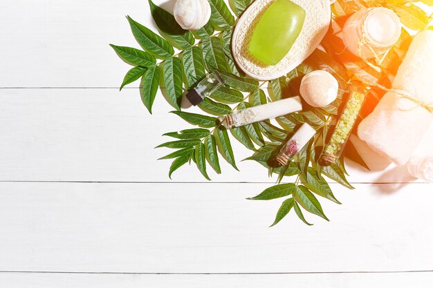 Spa set with towel and soap on white wooden background with green leaves sun flare