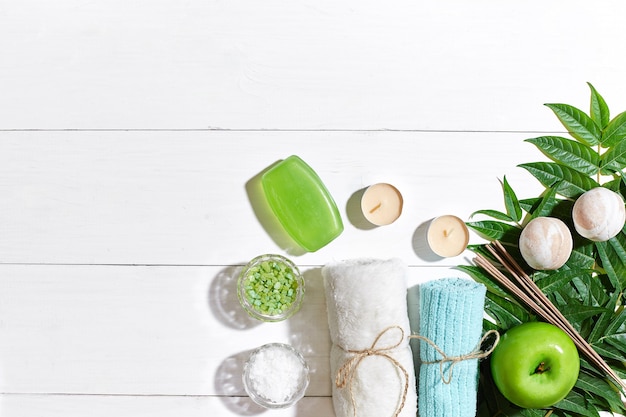 Photo spa set with towel and soap on white wooden background with green leaves