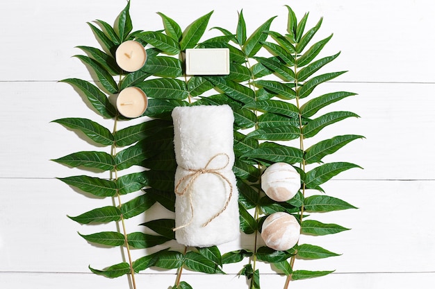 Spa set with towel and soap on white wooden background with green leaves