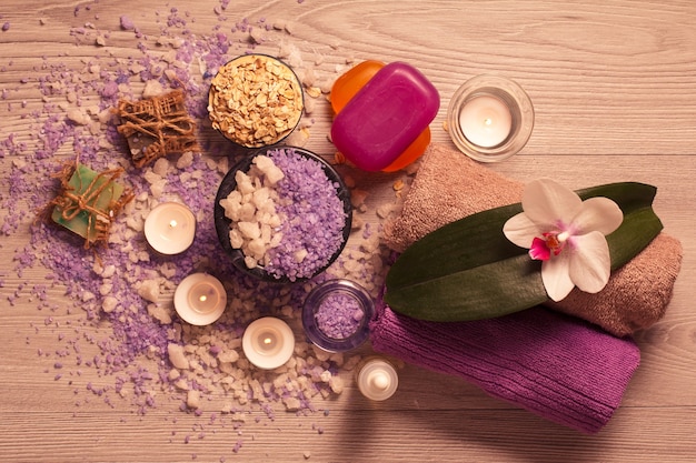 Ambiente termale con fiori di orchidea, ciotola con sale marino, sapone aromatico, scrub, candele e asciugamani su tavola di legno