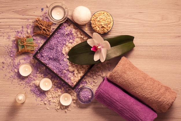 Ambiente termale con fiori di orchidea, scatola con sale marino, sapone aromatico, scrub, candele e asciugamani su tavola di legno