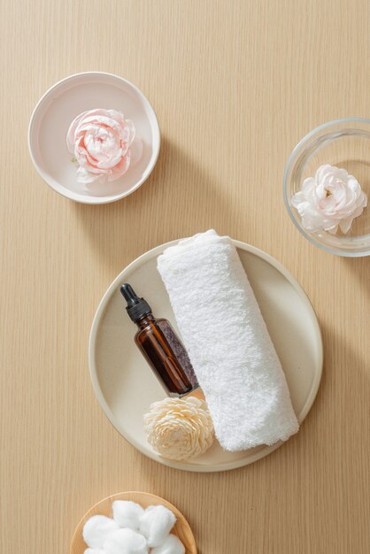 Spa setting with towel and essential oil on plate and flowers on wooden background