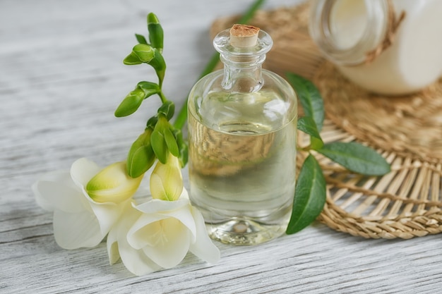 Spa ancora in vita con profumo e bottiglia di olio aromatico circondato da fiori di fresia, sulla superficie chiara