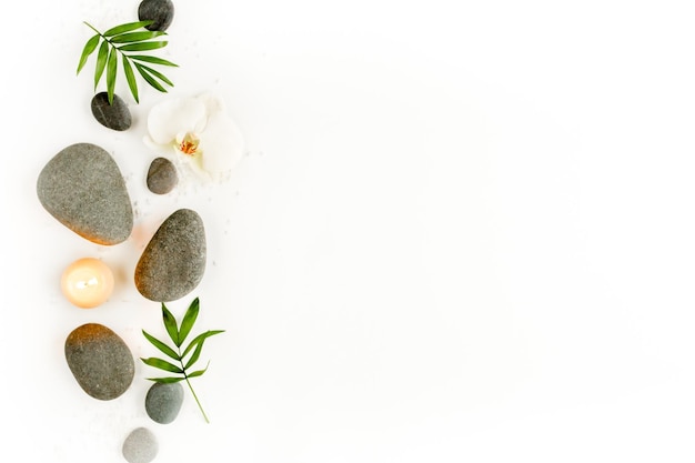 Spa stones palm leaves flower white orchid candle and zen like grey stones on white background Flat lay top view