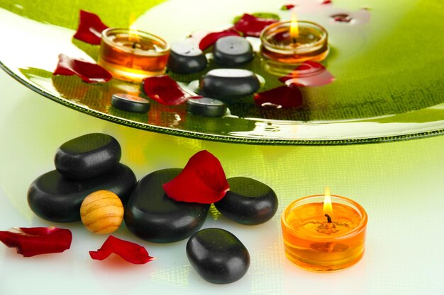 Spa stones with rose petals and candles in water on plate isolated on white