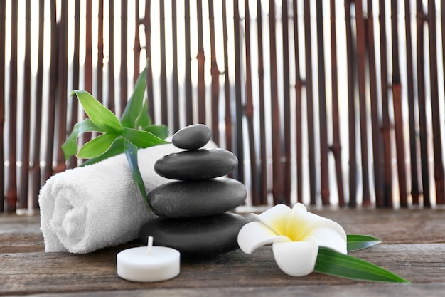 Spa stones with towel, bamboo, candle and tropical flower on wooden surface