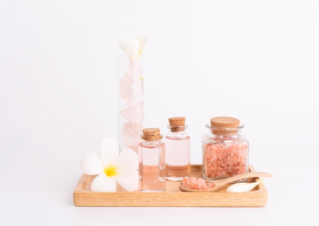 Spa treatment with rose liquid soap, pink salt, stones and Plumeria flower on wooden tray over white