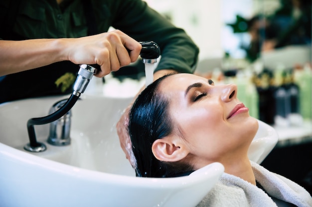 Spa treatments. Top view of hairdresserâs hands washing hair of her customer in salon before the hairstyling process.