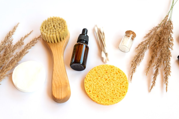 Spa and wellness concept with sea salt, dry pampas, brush, oil and face sponges on white background, top view