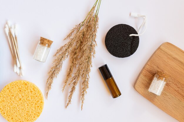 Spa and wellness concept with sea salt, dry pampas, brush, oil and face sponges on white background, top view.