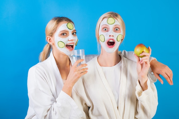 Photo spa and wellness. girls friends sisters making clay facial mask. anti age mask. stay beautiful. skin care for all ages. women having fun cucumber skin mask. drink water eat fruits. health concept.