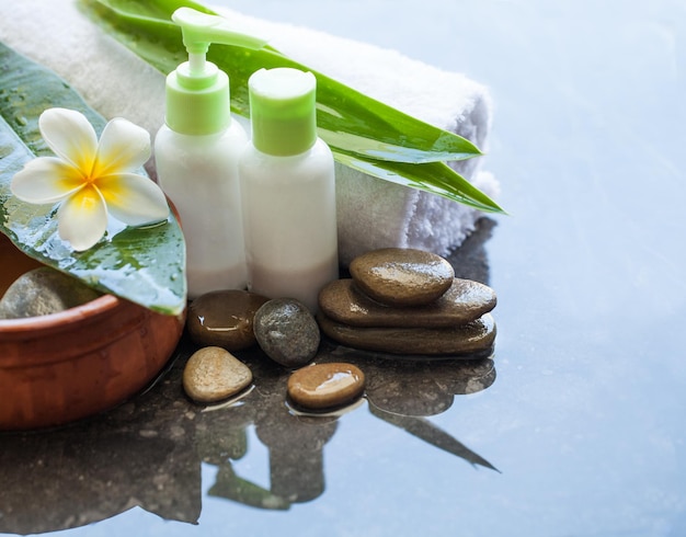 Spa or wellness setting with bowl of water with flower towel and cream tubes on dark background