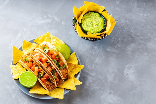 Spaans mexicaans eten. bord met taco's en tortillachips op een grijze achtergrond. mexicaanse taco, nacho chips en guacamole saus. ruimte kopiëren. bovenaanzicht