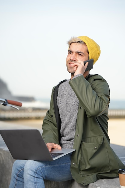 Spaanse freelancer die op zijn telefoon praat en laptop buitenshuis gebruikt