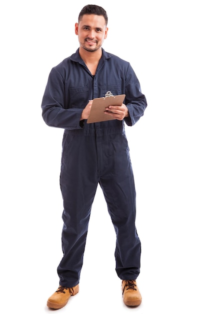 Foto spaanse jonge elektricien die overall draagt en een checklist op een witte achtergrond bekijkt