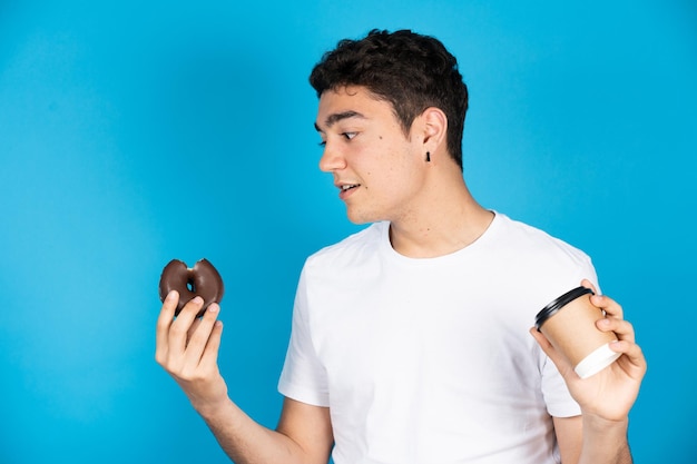 Spaanse jonge man met recyclebare kop koffie en chocolade donut geïsoleerd op blauwe achtergrond