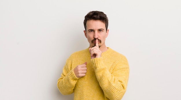 Spaanse jongeman die er serieus uitziet en kruist met de vinger tegen de lippen gedrukt en vraagt om stilte of stilte om een geheim te bewaren