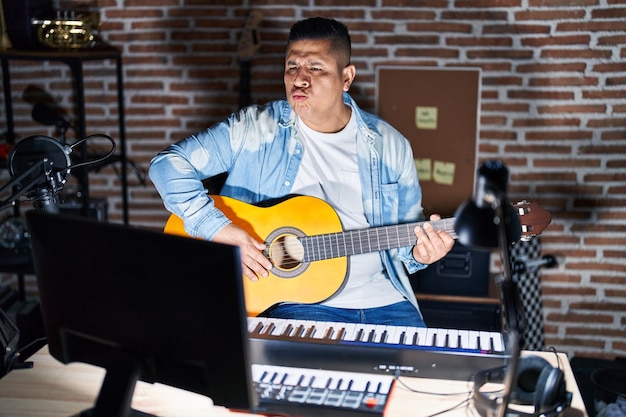 Spaanse jongeman die klassieke gitaar speelt in de muziekstudio en naar de camera kijkt terwijl hij een kus in de lucht blaast en mooi en sexy is. liefde uitdrukking.