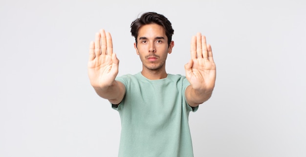 Spaanse knappe man die er serieus, ongelukkig, boos en ontevreden uitziet en de toegang verbiedt of stop zegt met beide open handpalmen