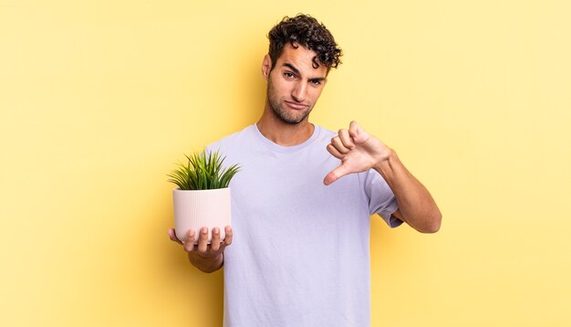 Spaanse knappe man die zich boos voelt en duimen naar beneden laat zien. decoratief plantenconcept