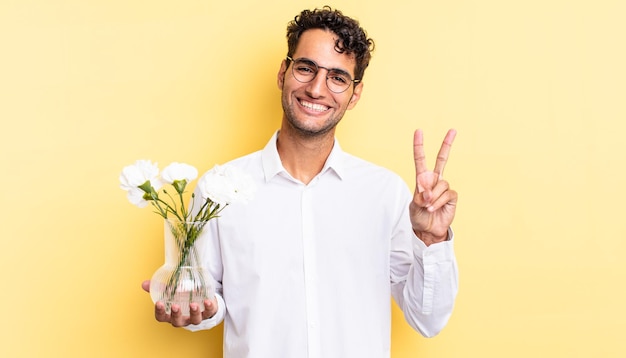 Spaanse knappe man lacht en ziet er gelukkig uit, gebarend overwinning of vrede. bloemen pot concept