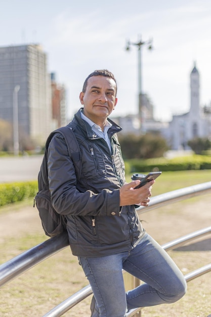 Spaanse man die zijn mobiele telefoon gebruikt en op een reling leunt in een openbaar park