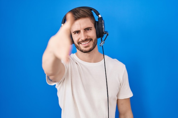 Spaanse man met baard die naar muziek luistert met een koptelefoon die vriendelijk glimlacht en handdruk aanbiedt als begroeting en succesvol bedrijf verwelkomt