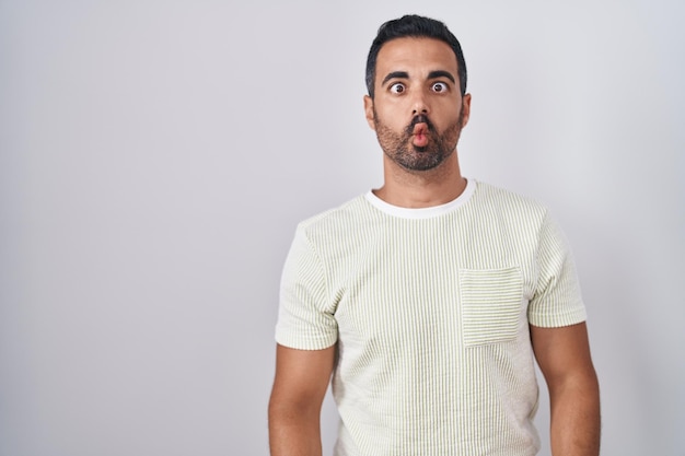 Spaanse man met baard die over een geïsoleerde achtergrond staat en een visgezicht maakt met lippen, een gek en komisch gebaar. grappige uitdrukking.