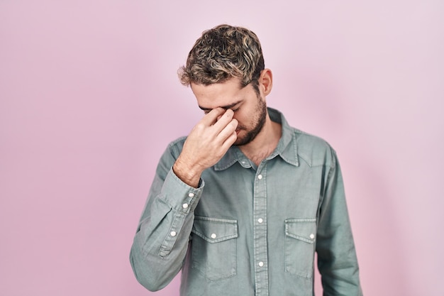 Spaanse man met baard staande over roze achtergrond moe wrijven neus en ogen gevoel vermoeidheid en hoofdpijn stress en frustratie concept