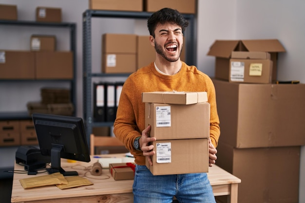 Spaanse man met baard werkt bij e-commerce voor kleine bedrijven met pakketten boos en boos schreeuwend gefrustreerd en woedend schreeuwend van woede woede en agressief concept