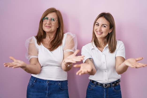 Foto spaanse moeder en dochter dragen casual wit t-shirt over roze achtergrond glimlachend vrolijk handen aanbiedend hulp en acceptatie.