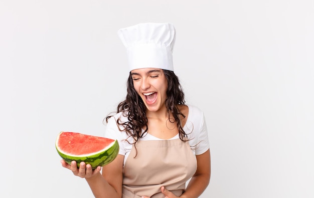 Spaanse mooie chef-kokvrouw die hardop lacht om een hilarische grap en een watermeloen vasthoudt